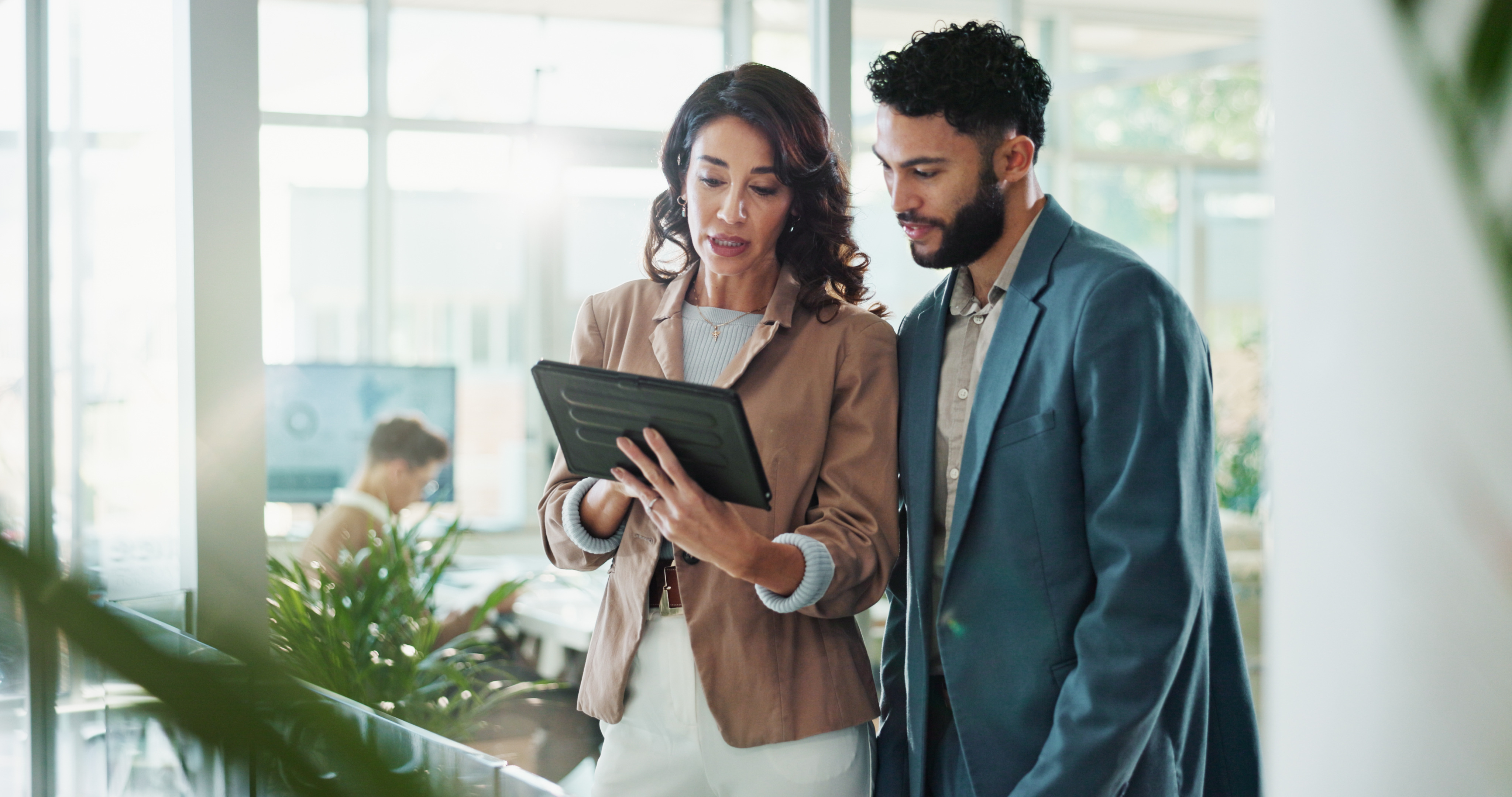 Two business professionals reviewing information on a tablet in a bright, modern office environment, emphasizing teamwork and effective communication.