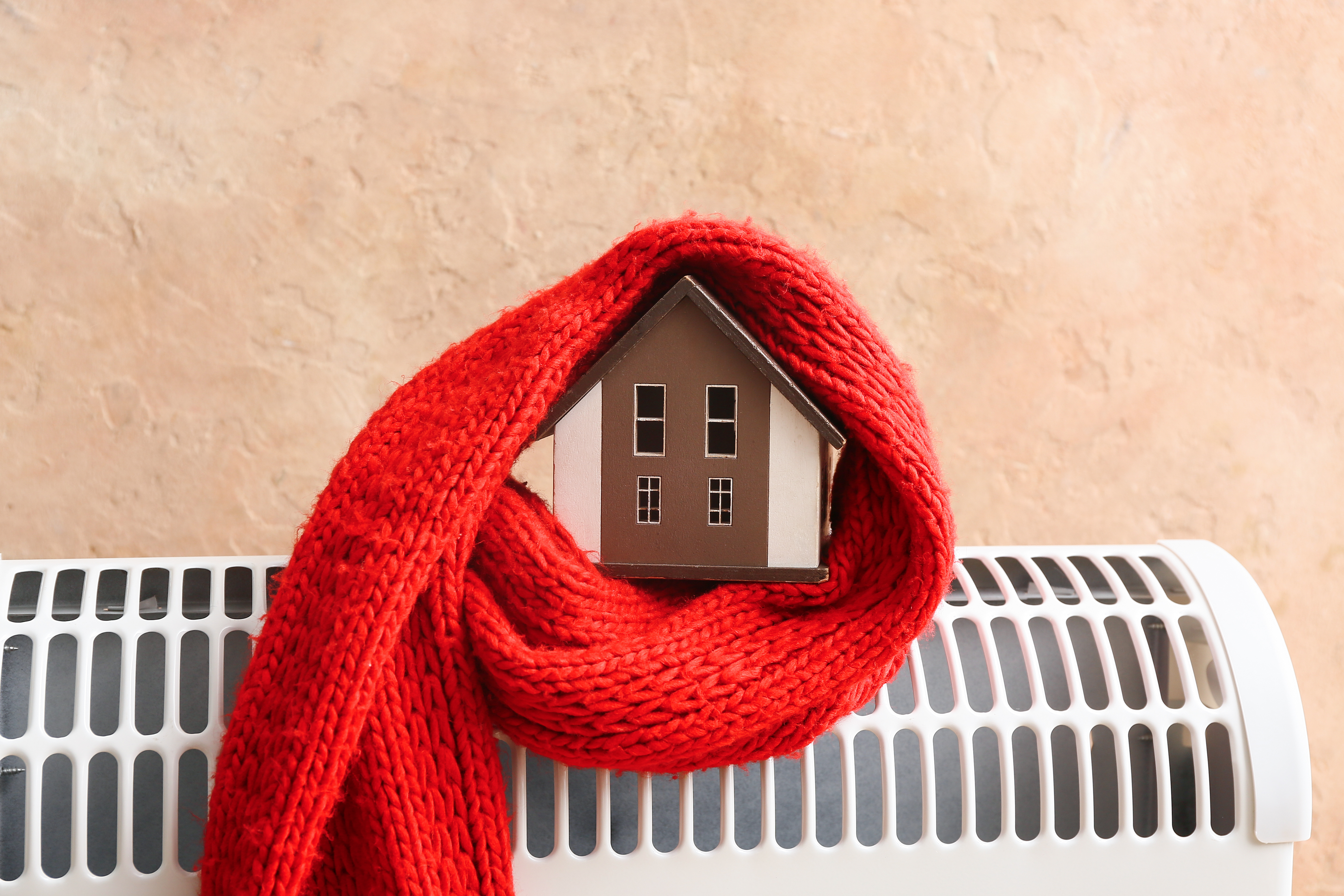 A small house model wrapped in a red scarf placed on a radiator, symbolizing home heating and energy efficiency