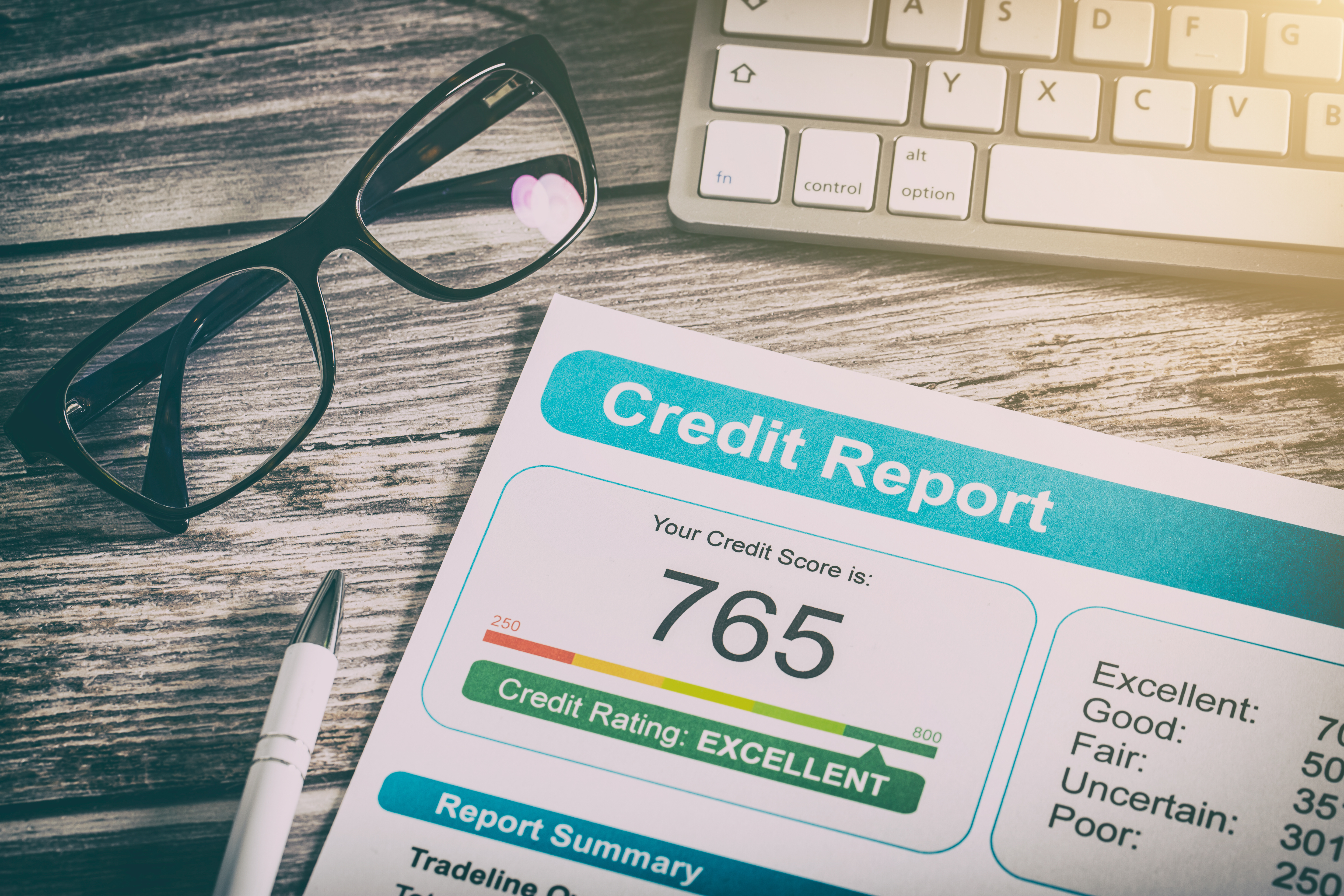 Credit report on a wooden surface. Next to it there are glasses, a keyboard and a pen. These attributes symbolize working on improving your credit score in order to get a loan.