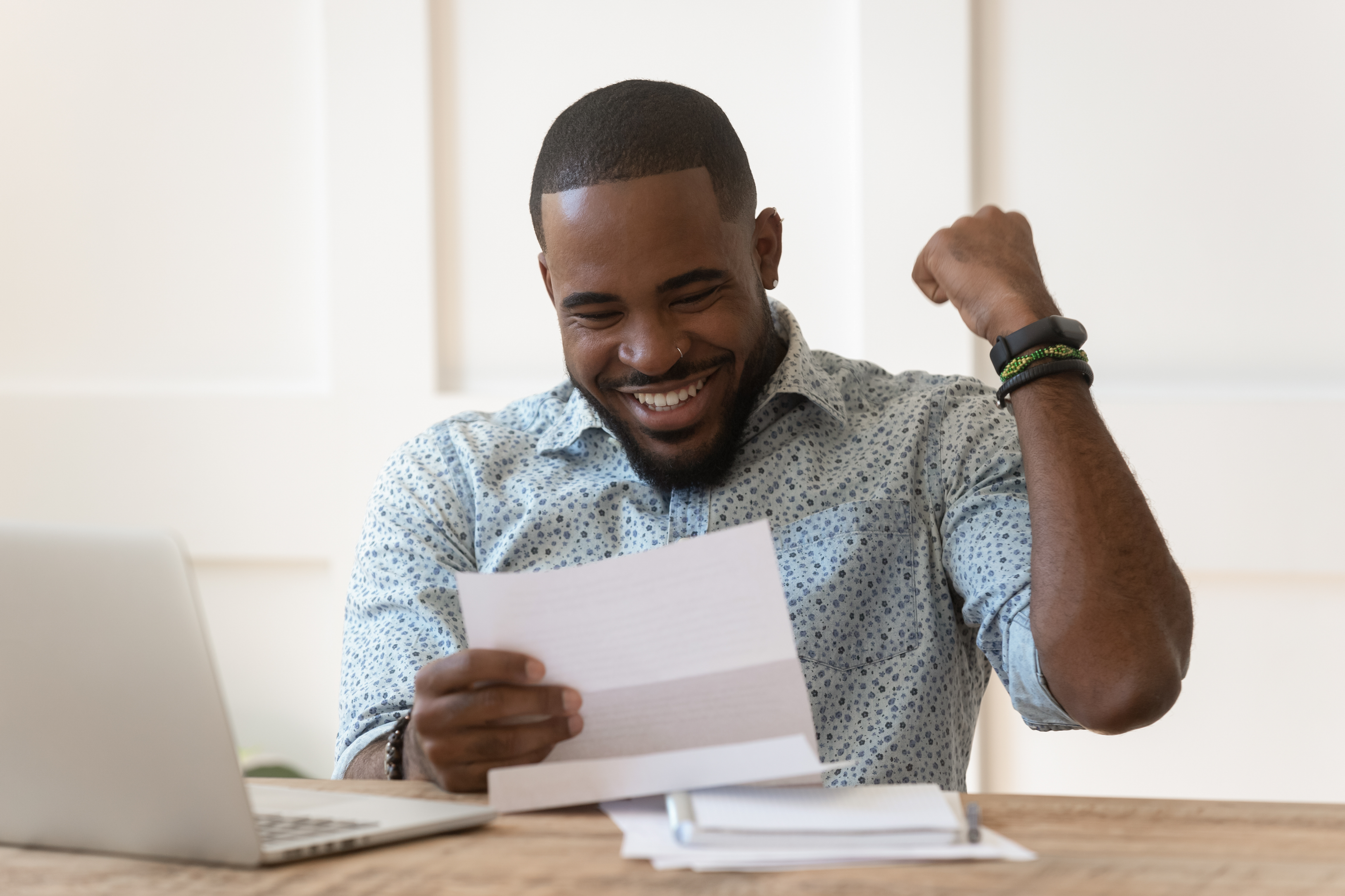 A happy young physician celebrates after reading a financial document, symbolizing successful student loan management and credit score improvement.