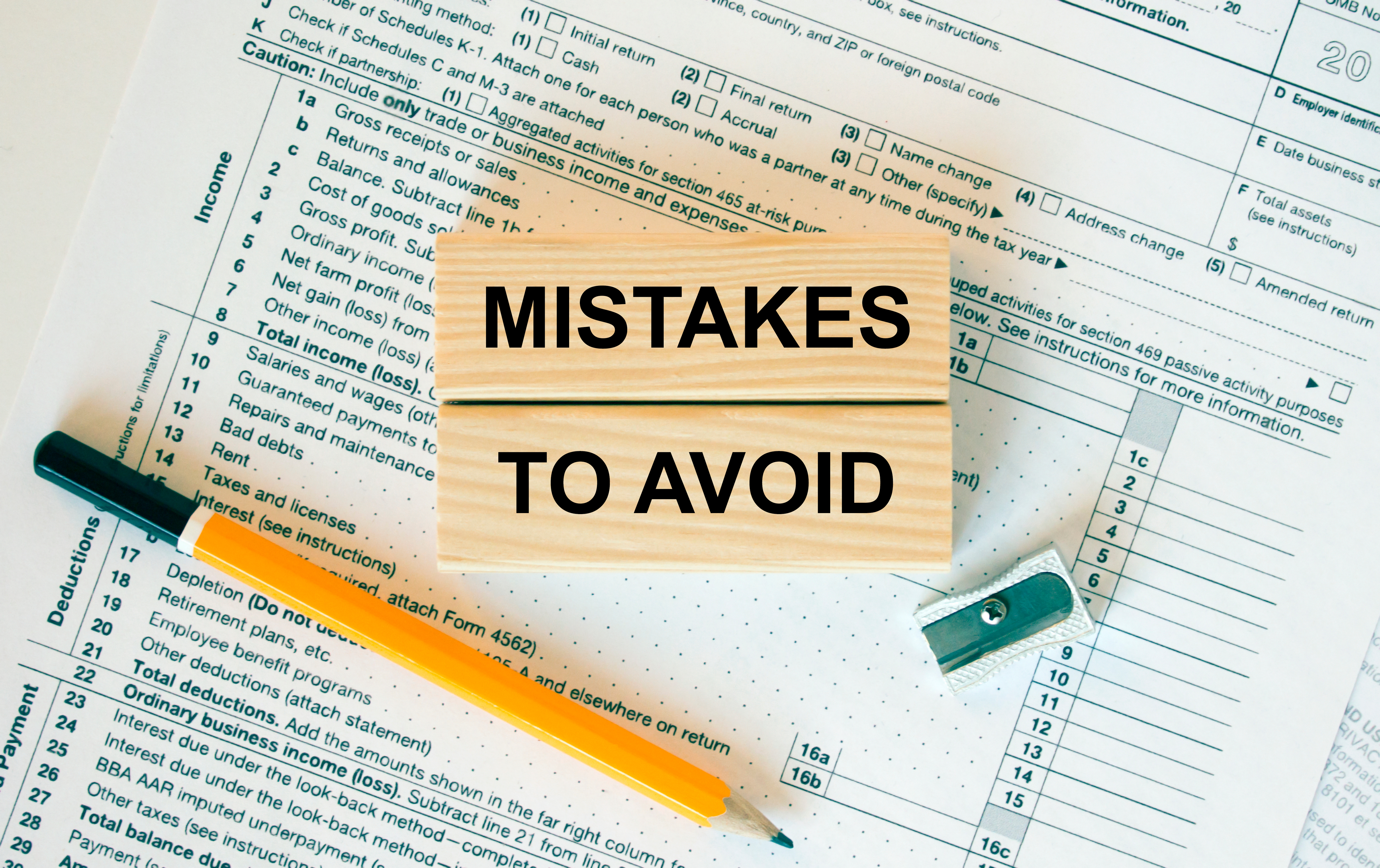 Wooden blocks with the text “Mistakes to Avoid” placed on top of a tax form, accompanied by a pencil and a sharpener.