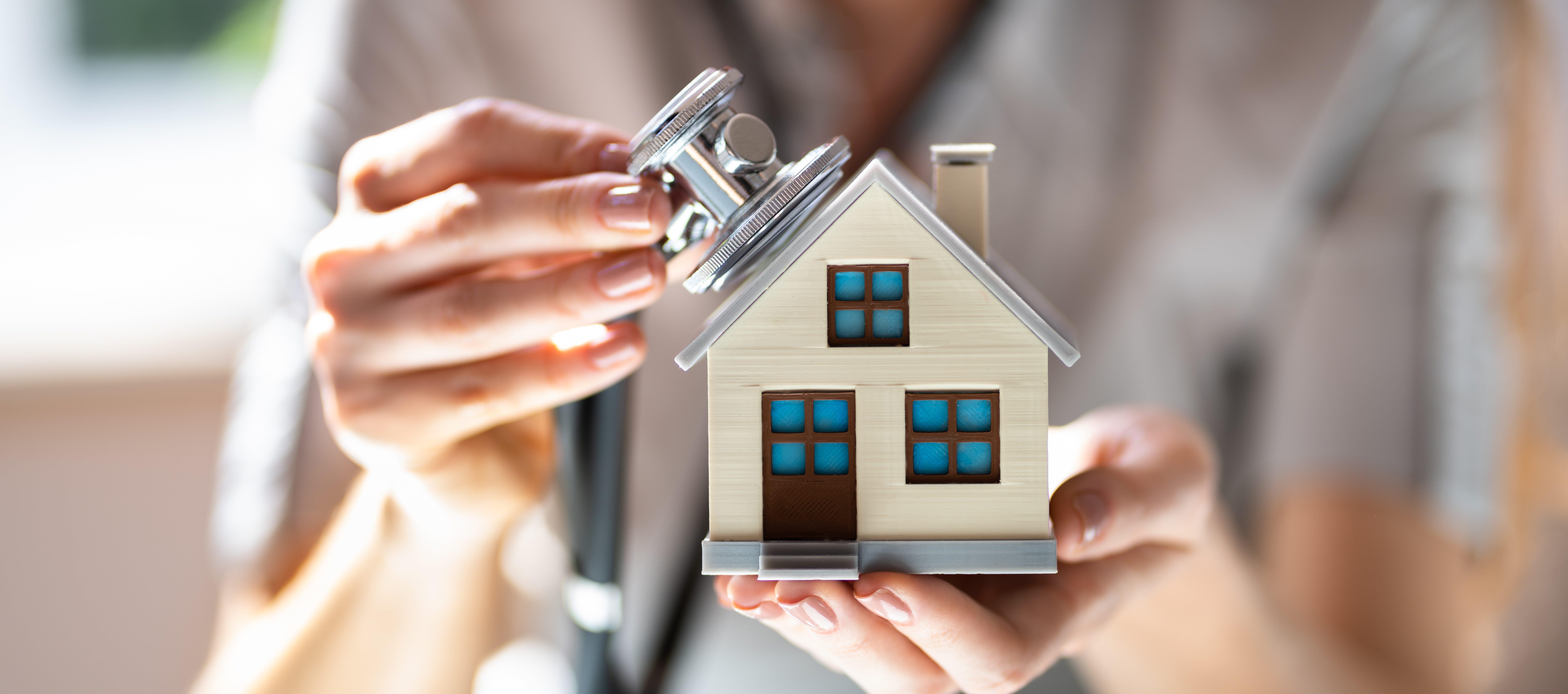 A doctor holding a small house model and examining it with a stethoscope, representing a medical professional considering buying a home.