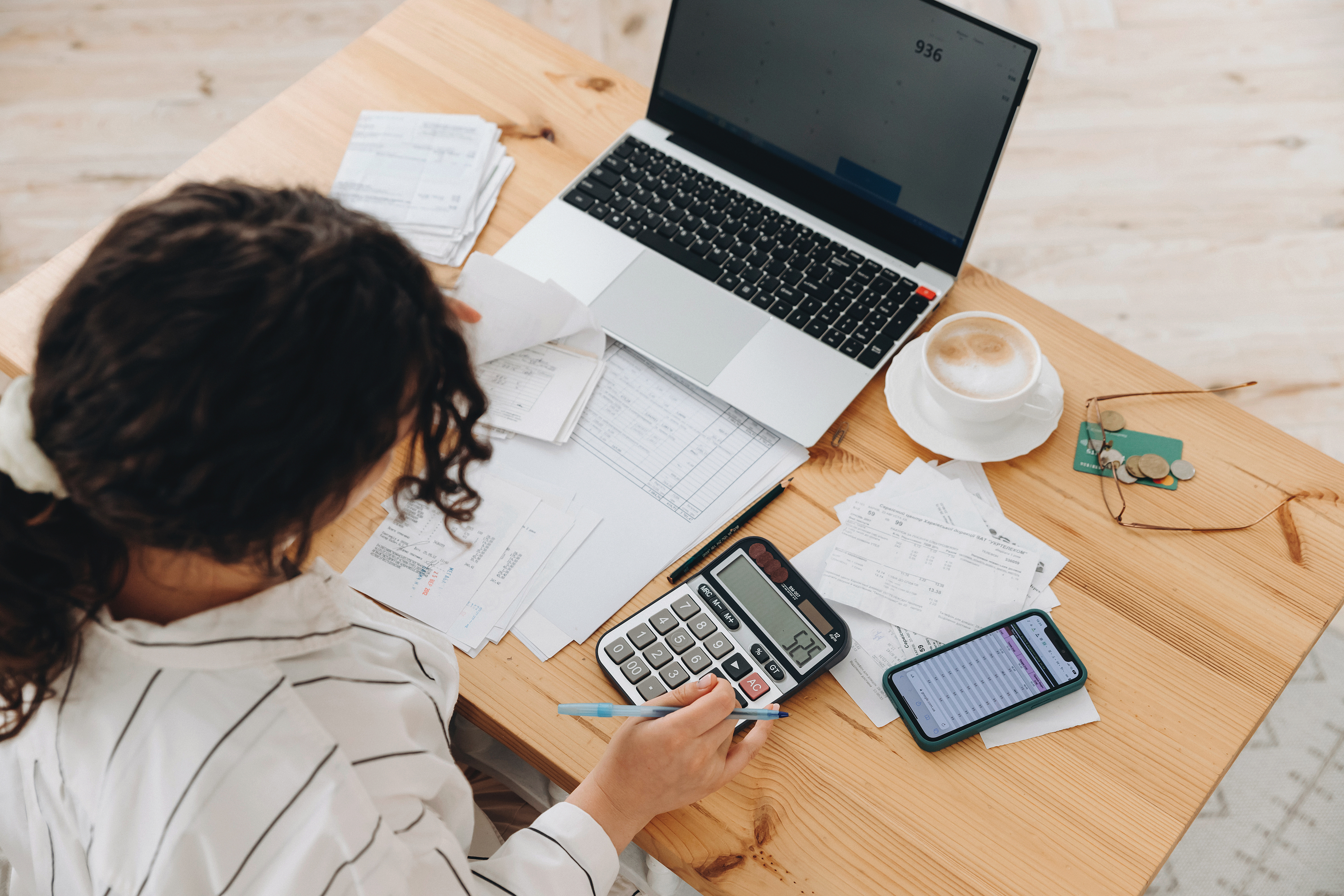 A physician reviewing financial documents, using a calculator and laptop to manage taxes and savings, with receipts and bills spread across a wooden desk.