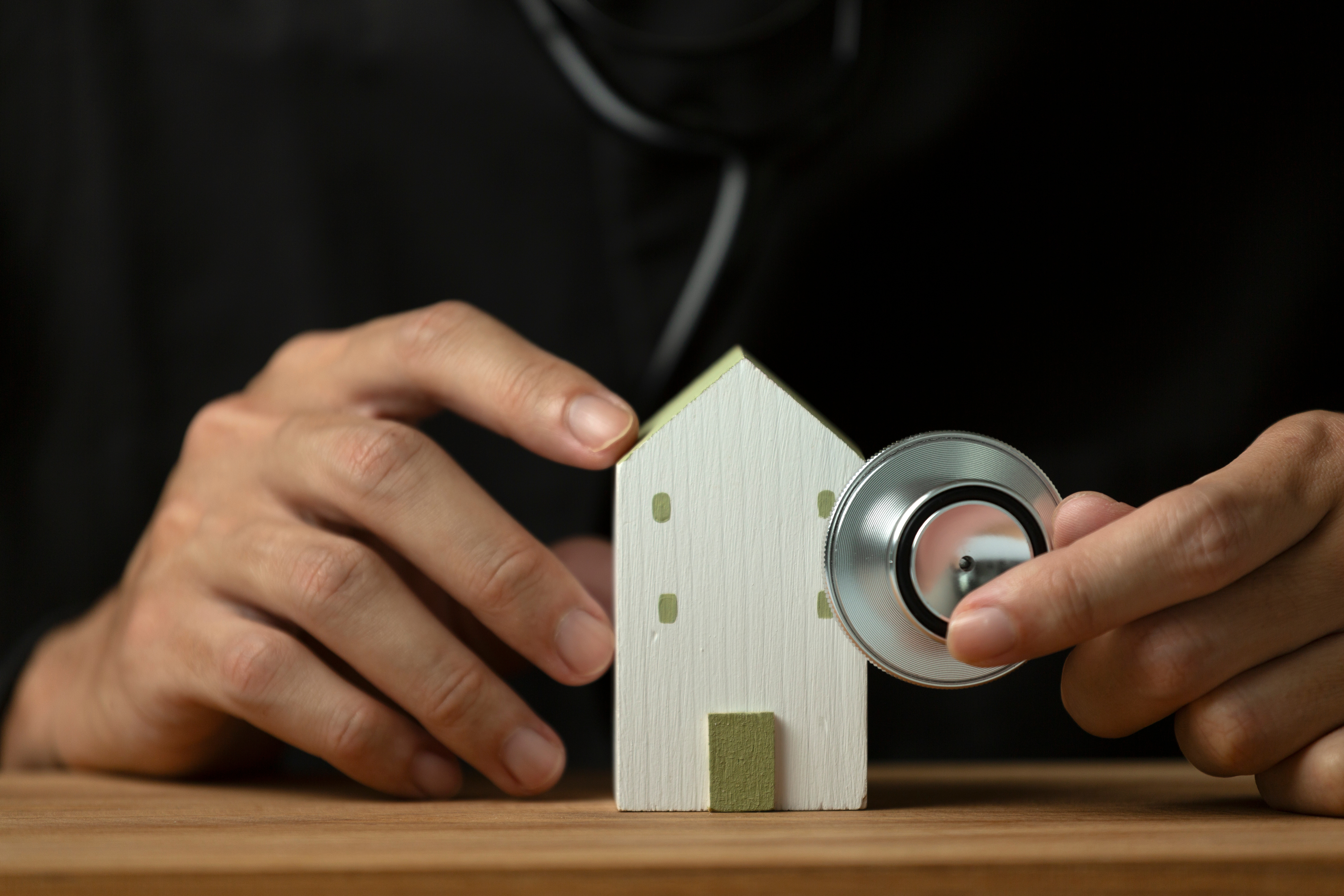 a doctor examining a figurine of a house with a stethoscope, which symbolizes financial health and choosing the right mortgage for doctors