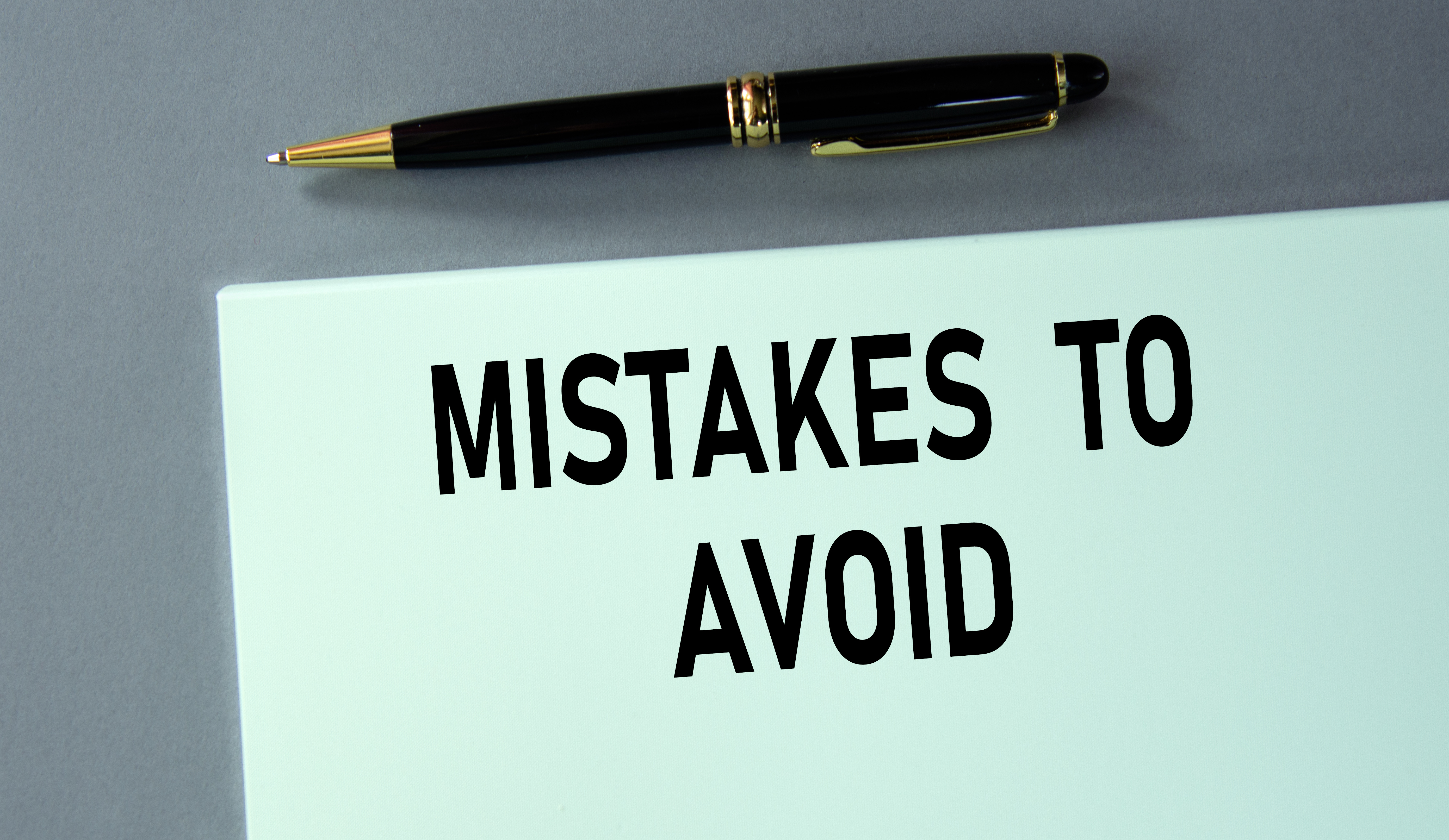 A pen placed above a mint green card with bold black text reading 'Mistakes to Avoid' on a gray background.